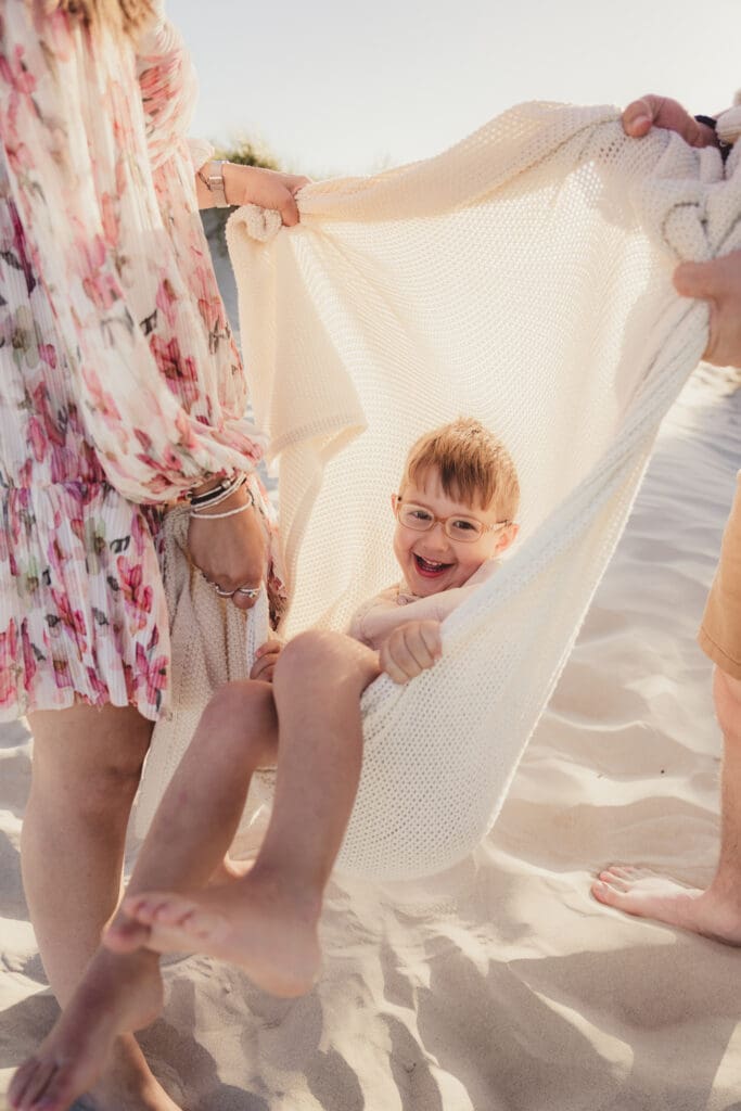 Boy laughing in blanket swing during fun family photos on west witterings beach