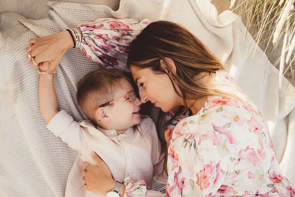 Mum and boy laying nose to nose on blanket on west witterings beach in west sussex, during family photoshoot