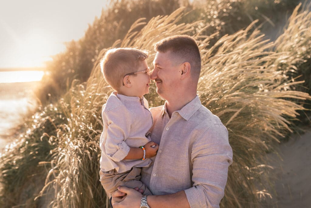 Dad holding boy with noses together smiling on west witterings beach during family photoshoot