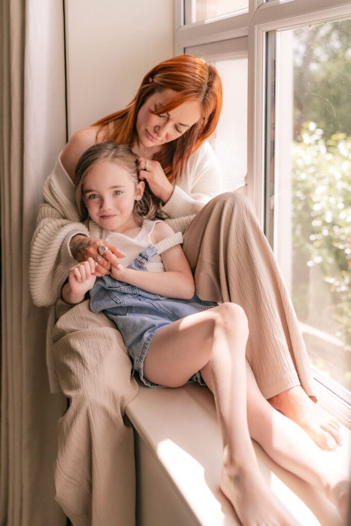 Relaxed mother-daughter moment by window captured naturally in Sussex at-home photoshoot