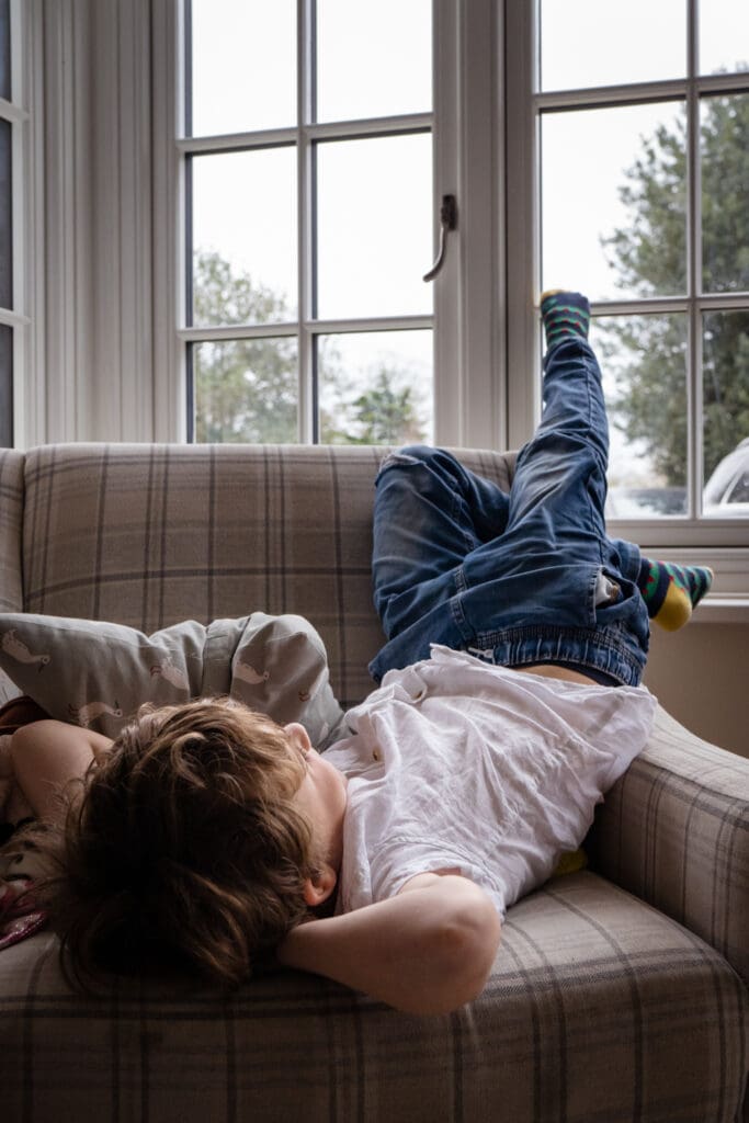 Boy relaxing upside down on sofa during home family photoshoot Sussex
