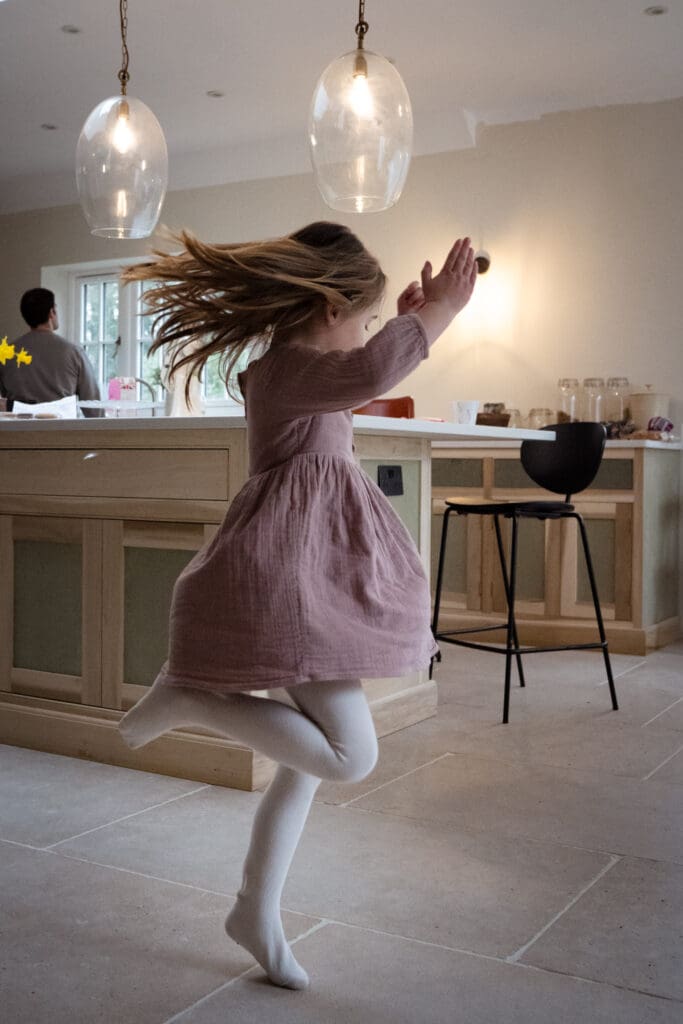Girl dancing and twirling in kitchen, relaxed at-home Sussex family photography