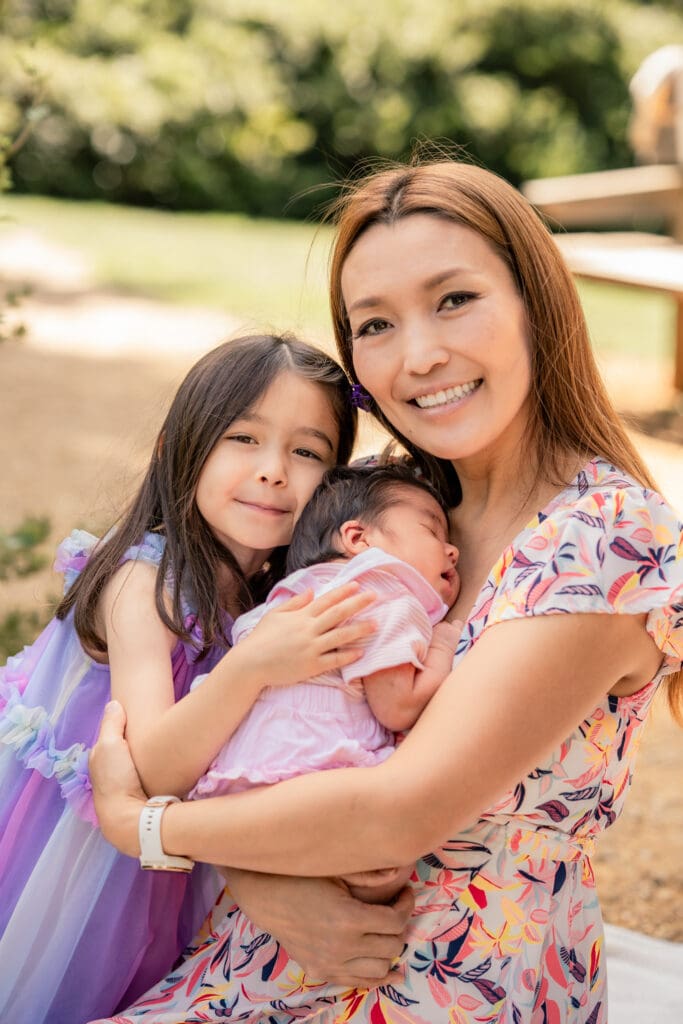 Mother cuddling newborn and daughter during relaxed outdoor family photoshoot in Sussex.
