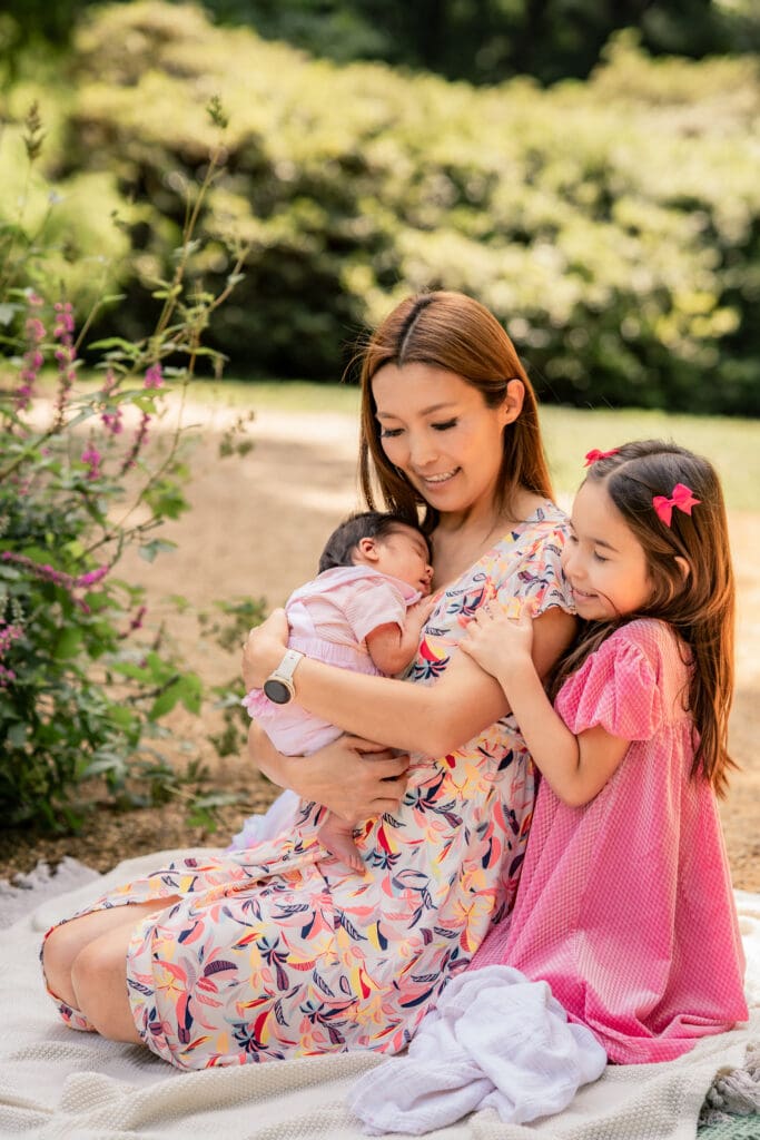 Big sister bonding with newborn baby during a relaxed garden photoshoot.