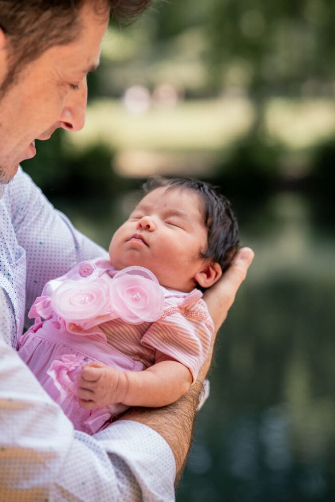Father holding newborn baby in arms during outdoor newborn photoshoot.