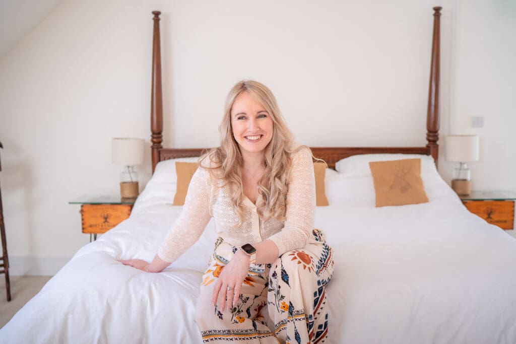 Branding photo of a woman in a relaxed, welcoming bedroom setting with soft natural light.