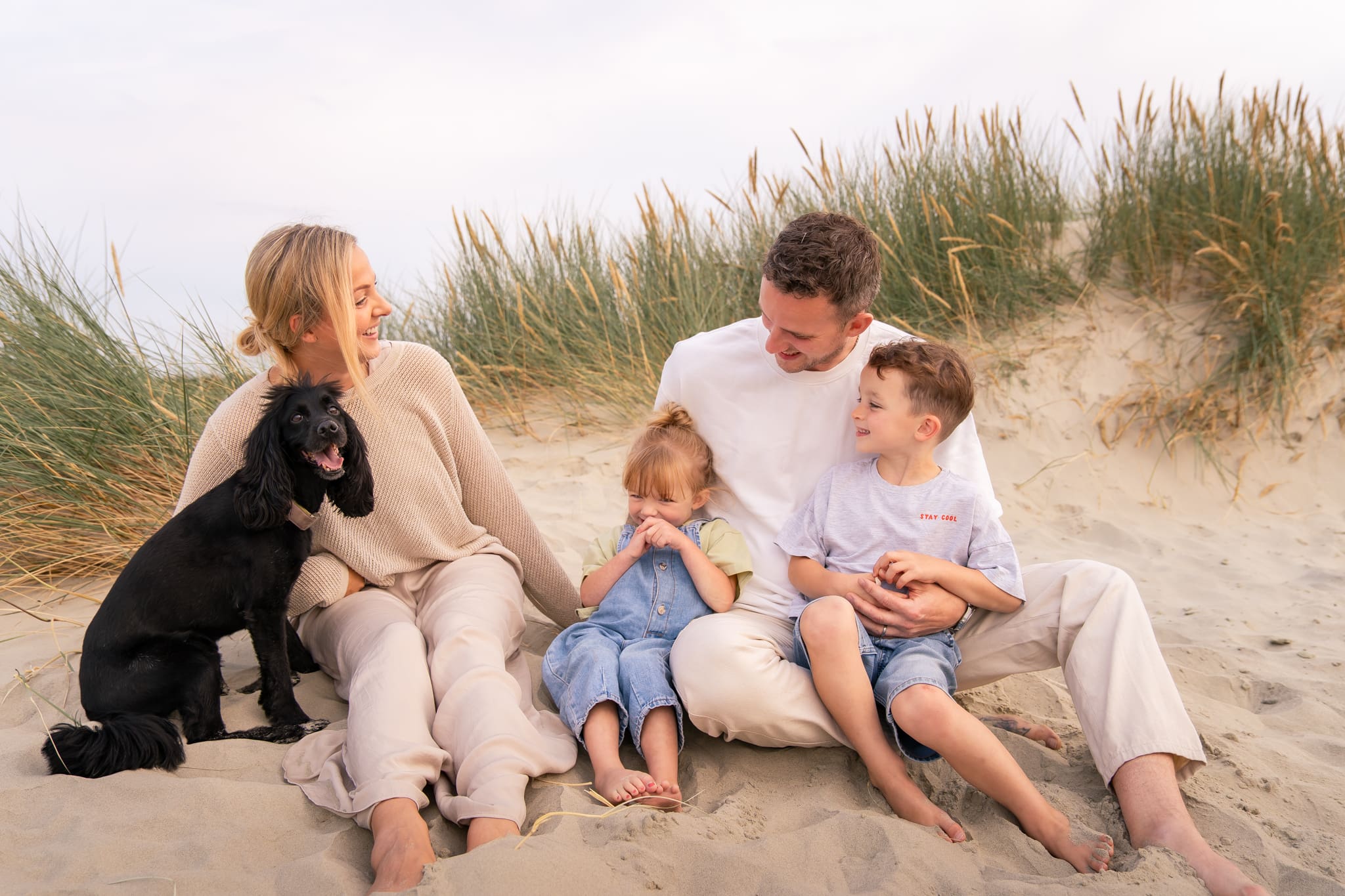 Candid family moment at West Wittering Beach with parents and children cuddling during golden sunset