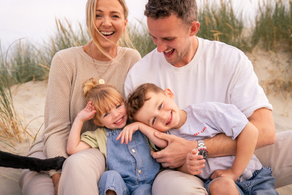 Candid family moment with parents and children laughing during a West Wittering Beach photoshoot.