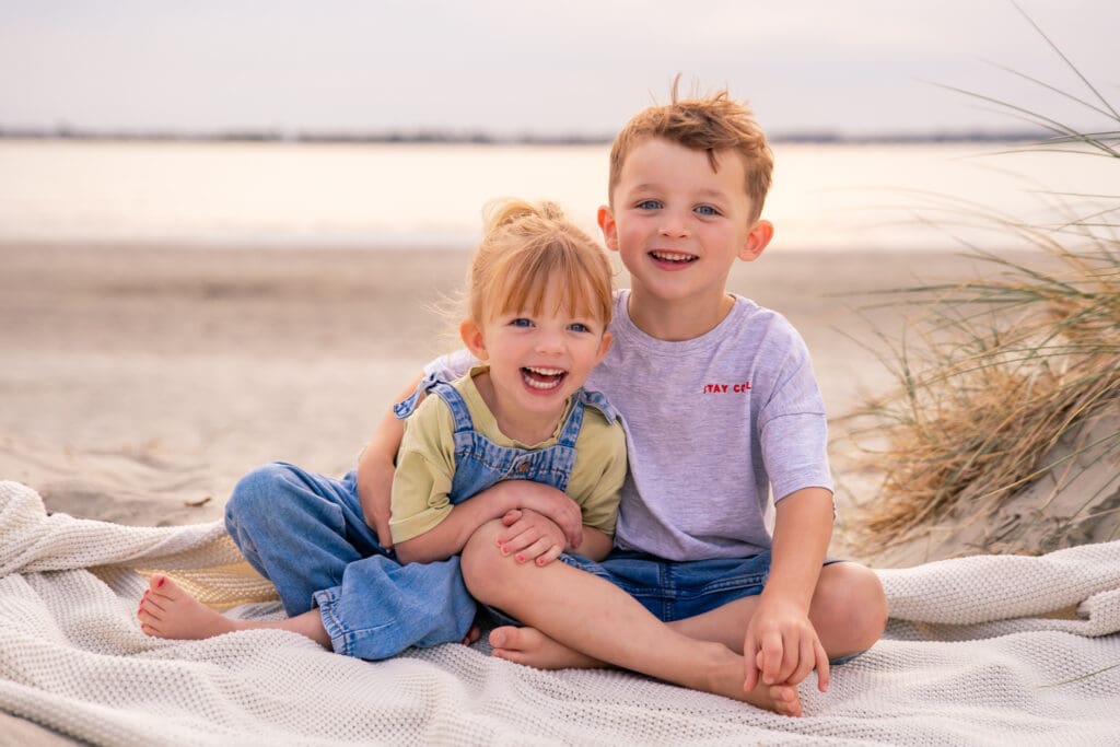 Two children smiling on a beach blanket during a West Sussex family photography session.