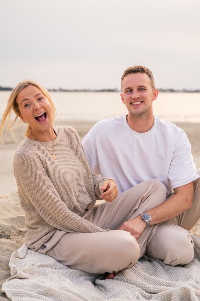 Relaxed couple sitting on a blanket at the West Sussex coast during a calm, golden-hour family shoot.