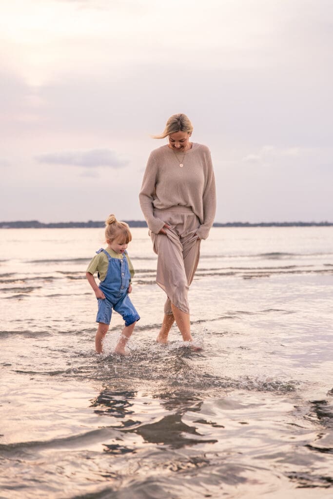 Adult and child walking barefoot in shallow water during a peaceful West Sussex family photoshoot.