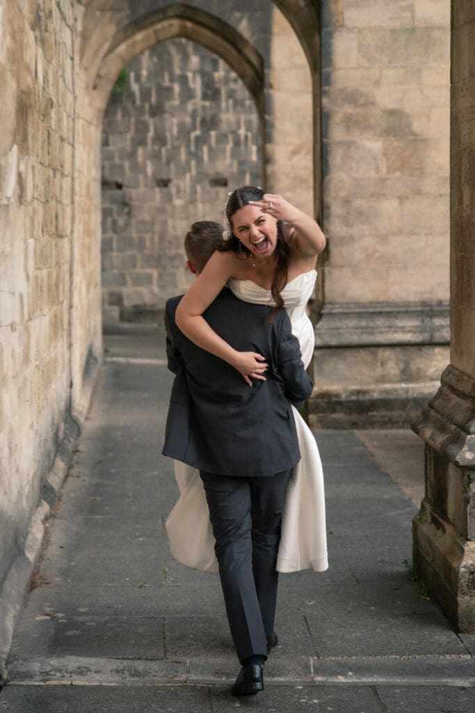 Groom carrying laughing bride through stone archway | fun natural wedding photography Sussex