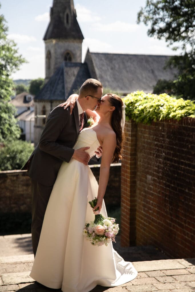 Bride and groom sharing a kiss with Sussex church in the background | romantic wedding photography Sussex