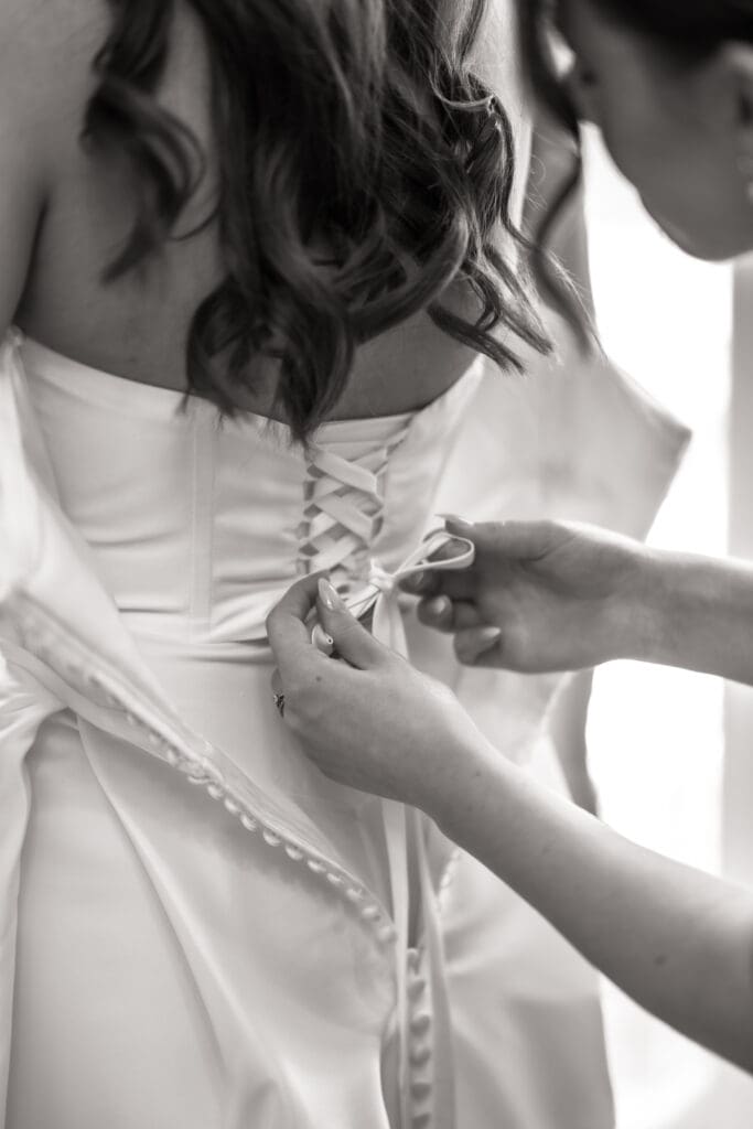 Bridesmaid lacing up bride's wedding dress during bridal preparations | Sussex wedding photographer