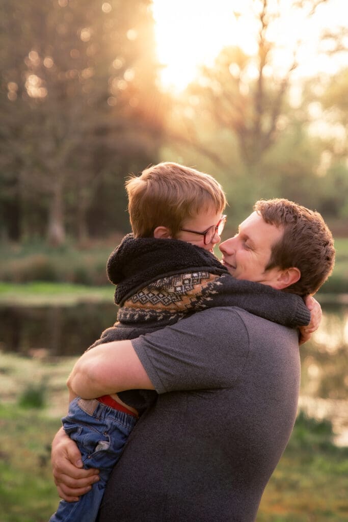 A father and son in glasses sharing a quiet, tender nose-to-nose moment, golden light glowing behind them