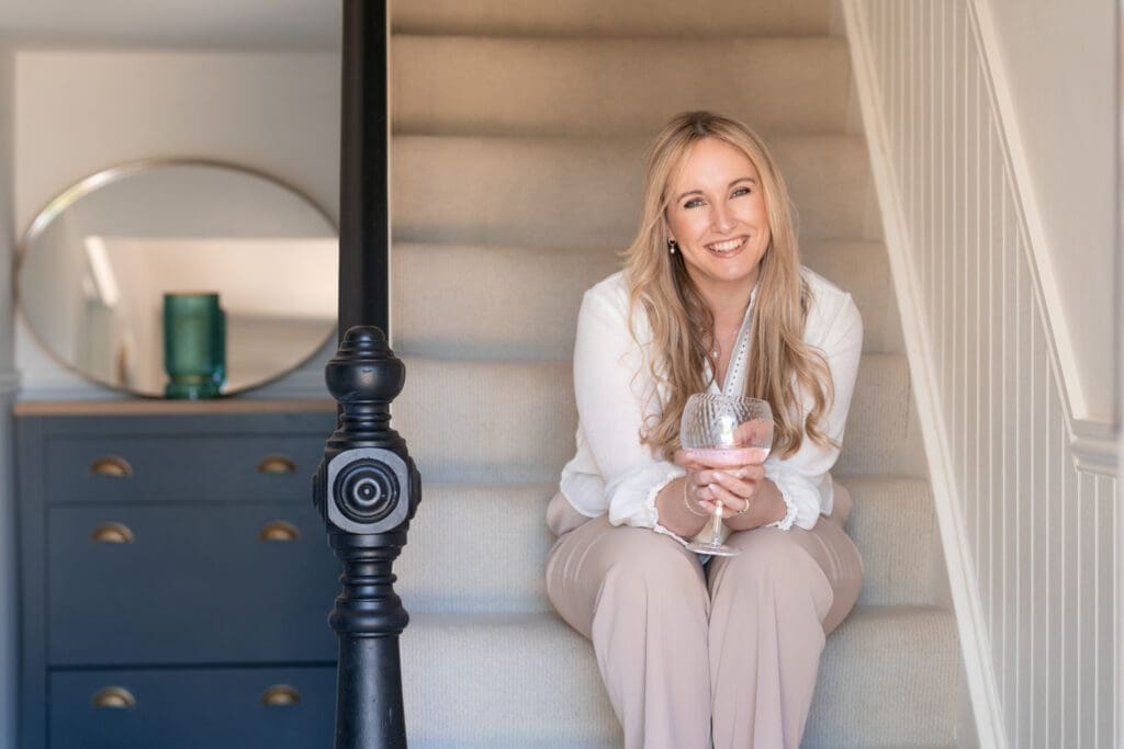Rachel Caws sitting on staircase with gin glass during branding shoot at coastal AirBnB in Rustington