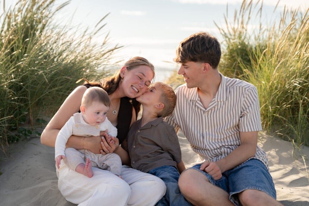 Parents laughing together with baby and toddler during a relaxed family photoshoot in the Sussex dunes.