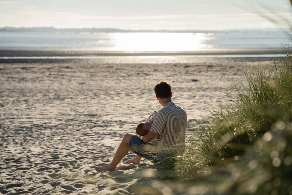 Two family members sitting quietly in the dunes, looking out to sea during a Sussex beach photoshoot.