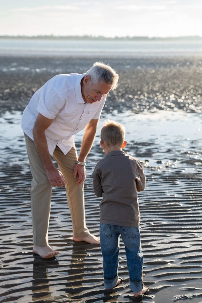 randad playing with toddler at the water's edge during a candid extended family photoshoot in Sussex.