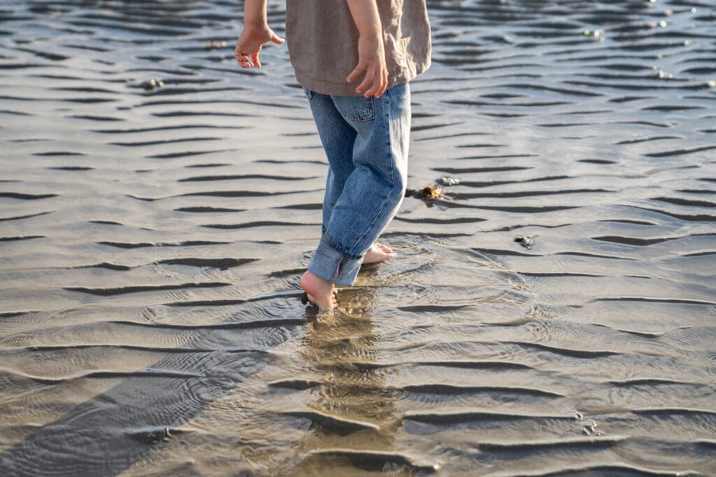 Family member walking along the wet sand shoreline at West Wittering Beach, Sussex.