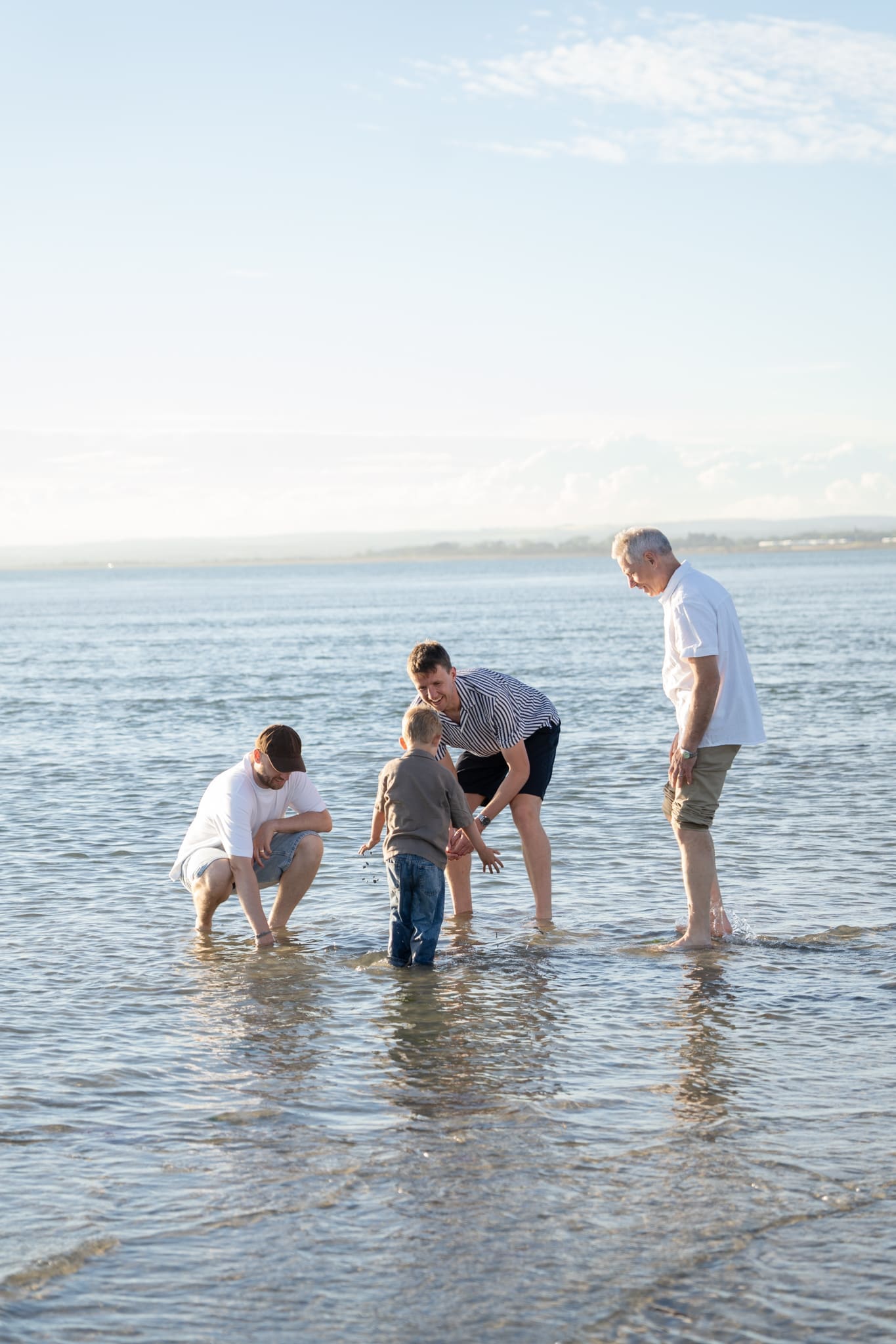 Family standing together at the shoreline as children play in the water at West Wittering Beach.