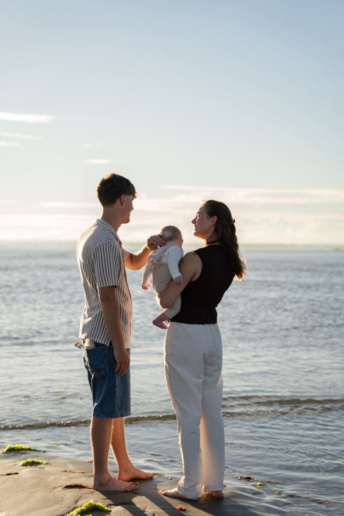 Dad holding baby while family gathers at the water's edge during an extended family photoshoot.