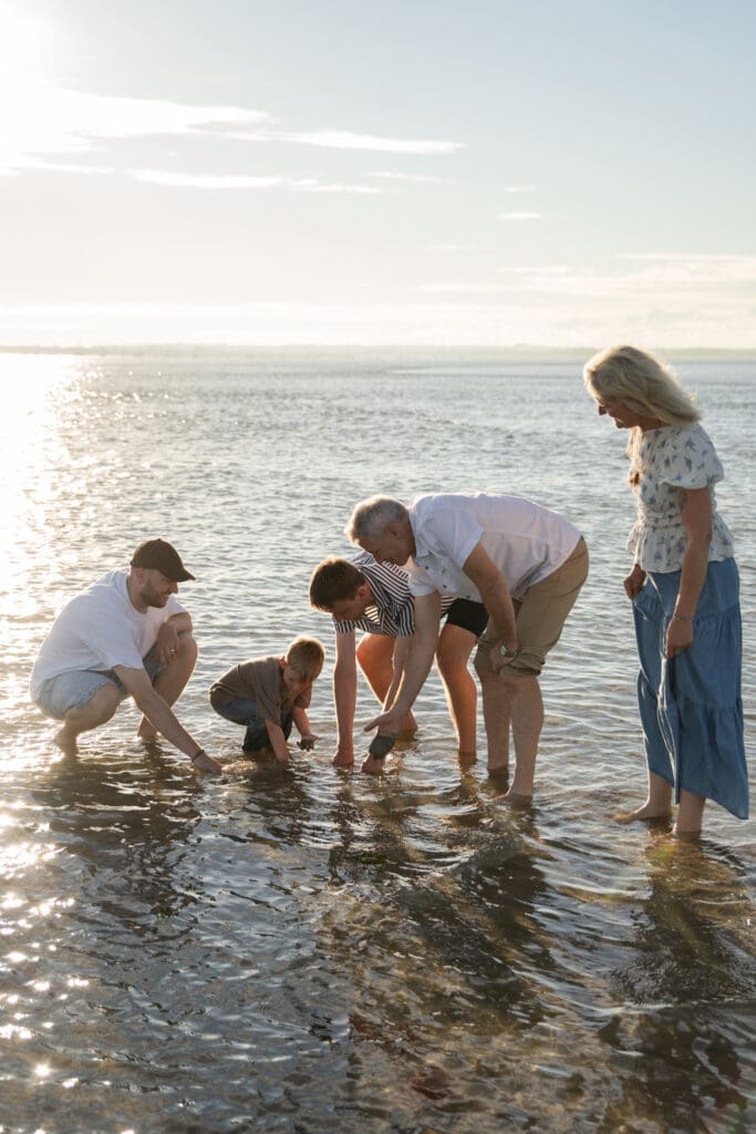 Grandad crouching down with toddler at the water's edge, West Wittering Beach.