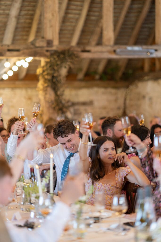 Wedding guests raising their glasses for a toast during the speeches inside Chapel Barn, Bolney