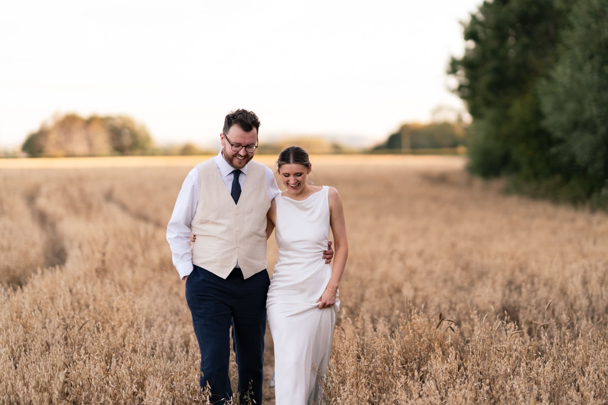 Bride and groom laughing together during golden hour couple portraits in a Sussex wheat field, taken by their Chapel Barn wedding photographer