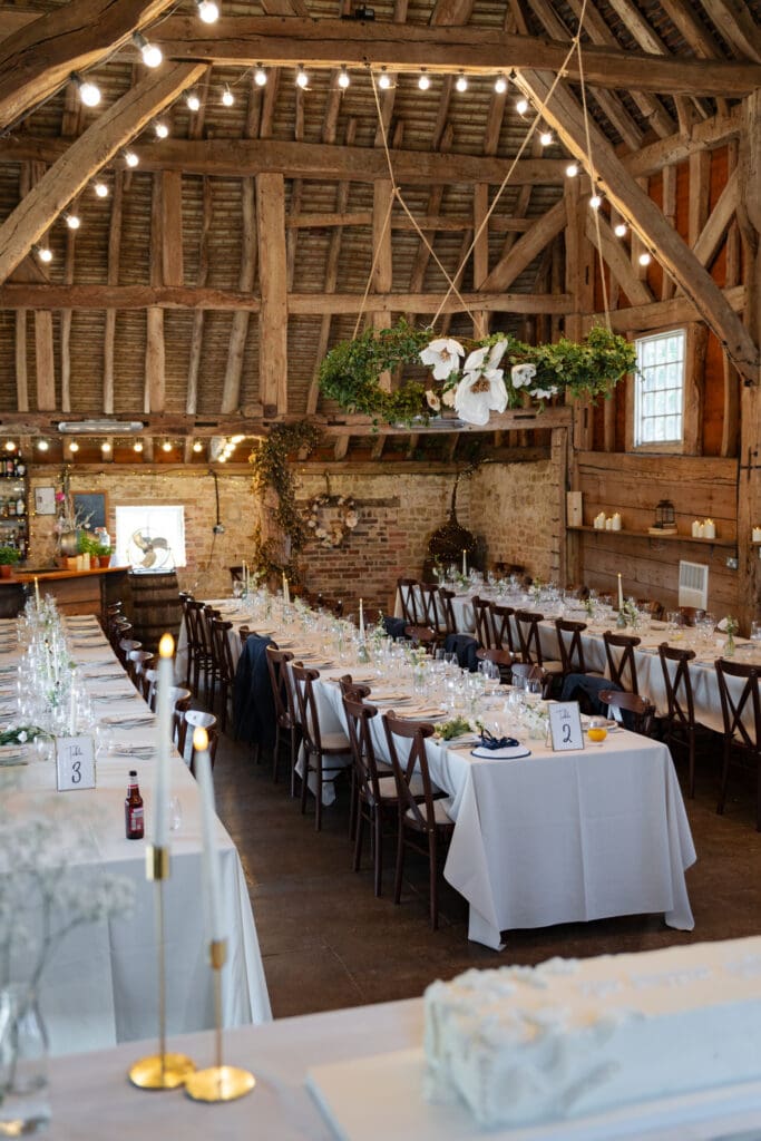 Rustic oak-beamed barn set for a wedding breakfast with long tables and a hanging foliage hoop at Chapel Barn in Bolney, Sussex