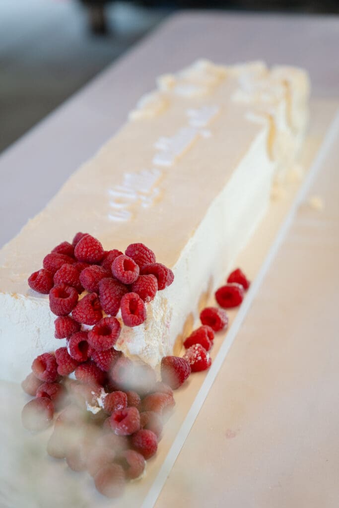 Long white semifreddo wedding cake topped with fresh raspberries on the table at Chapel Barn, Sussex