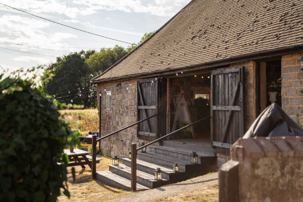Golden evening light on the stone barn exterior with candlelit steps and an open doorway at Chapel Barn in Bolney, Sussex