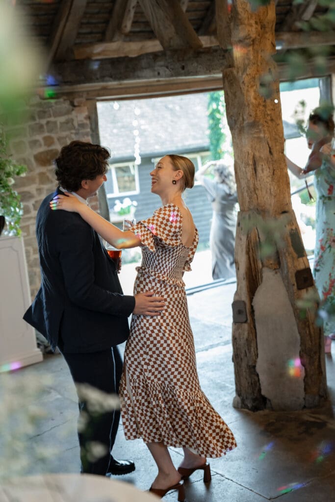Wedding guest laughing and dancing with a partner among the oak posts and festoon lights during the evening reception at Chapel Barn, Bolney