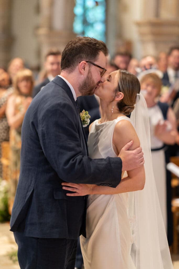 Bride and groom sharing their first kiss as a married couple during the ceremony at Holy Trinity Church, Cuckfield, Sussex