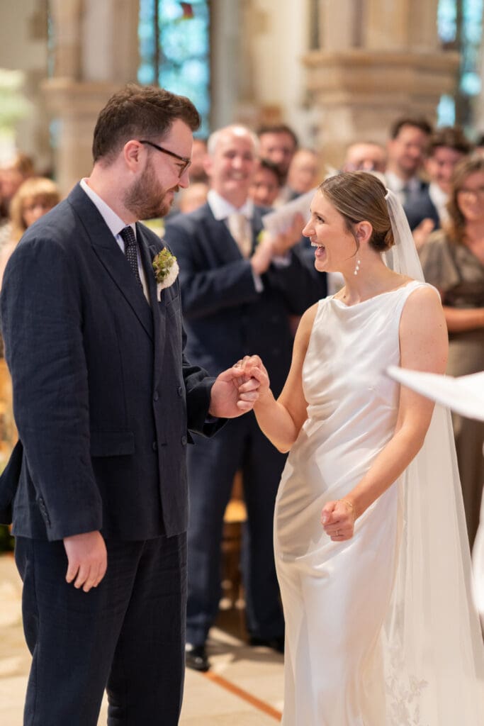 Bride laughing with delight as she and her groom hold hands at the altar, Holy Trinity Church, Cuckfield
