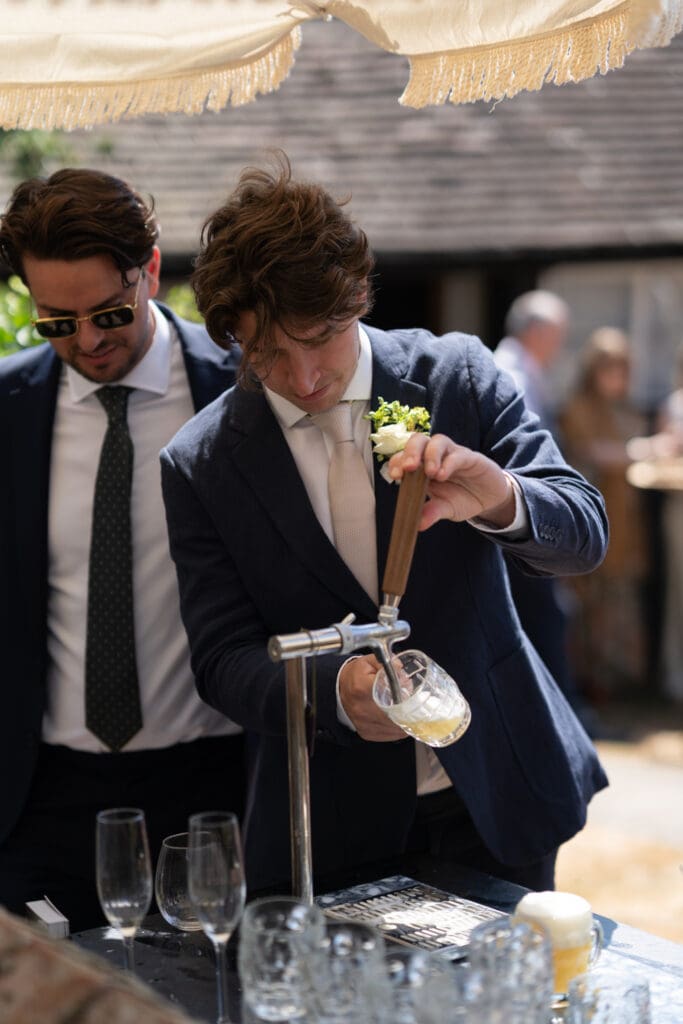 Guest pouring a beer at the outdoor bar during the sunny drinks reception at Chapel Barn, Sussex
