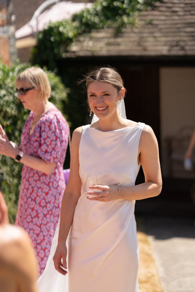 Bride smiling with a drink in hand during the drinks reception outside Chapel Barn, Bolney