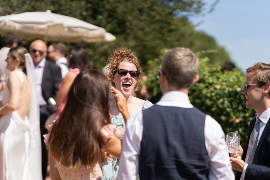 Wedding guest laughing during the outdoor drinks reception on a sunny day at Chapel Barn, Bolney
