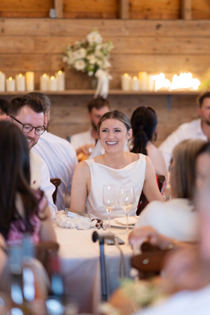 Bride laughing warmly during the speeches at the wedding breakfast inside Chapel Barn, Bolney