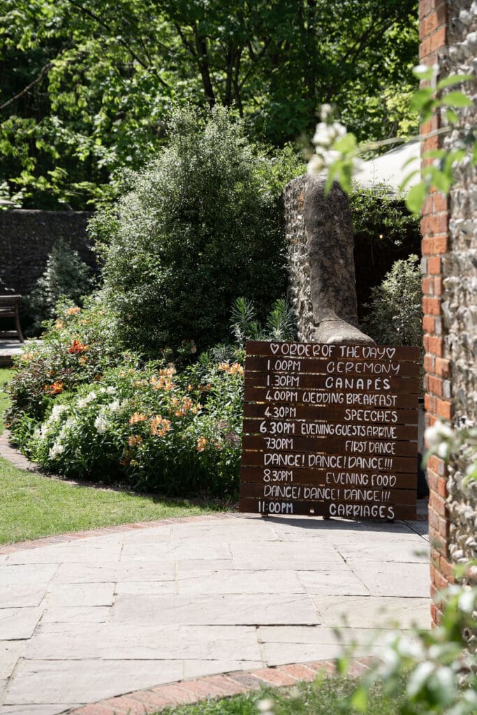 Wooden order of the day sign beside a flint wall in the gardens at Cissbury Barns
