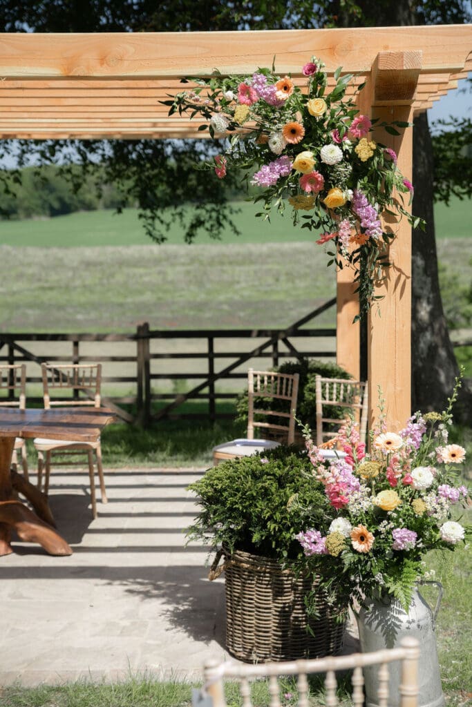 Wooden pergola dressed with pink, peach and lilac flowers, looking out over the fields
