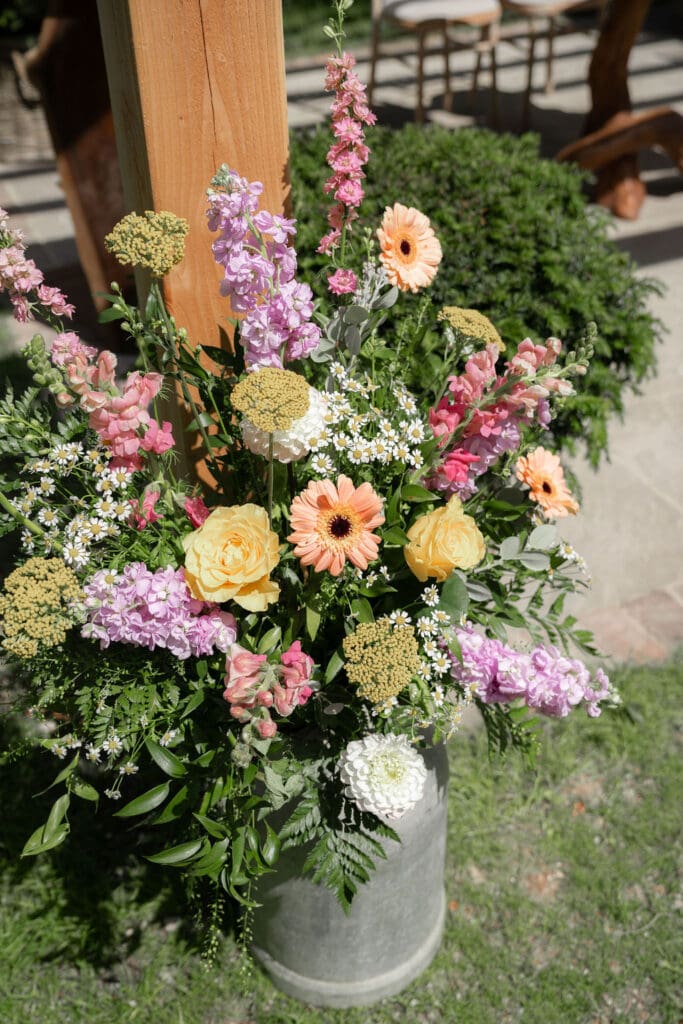 Milk churn filled with pink, peach and lilac flowers at the outdoor ceremony