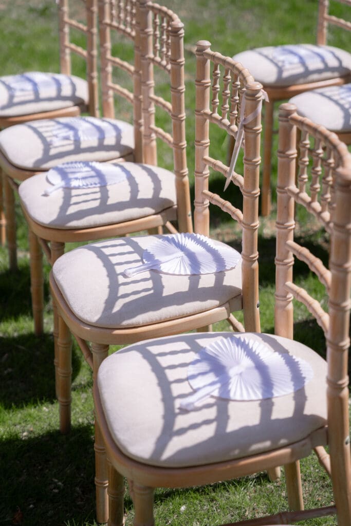 Rows of ceremony chairs with paper fans on each seat, casting striped shadows in the May sunshine