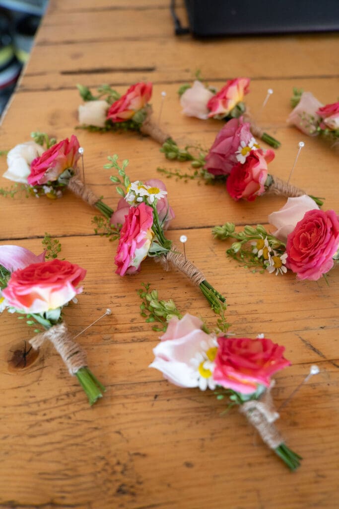Pink rose buttonholes laid out on a wooden table before the wedding