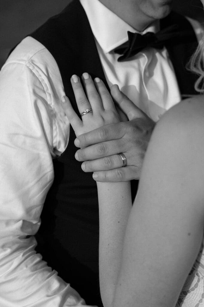 Black and white close-up of the bride's hand and wedding rings resting on the groom's chest