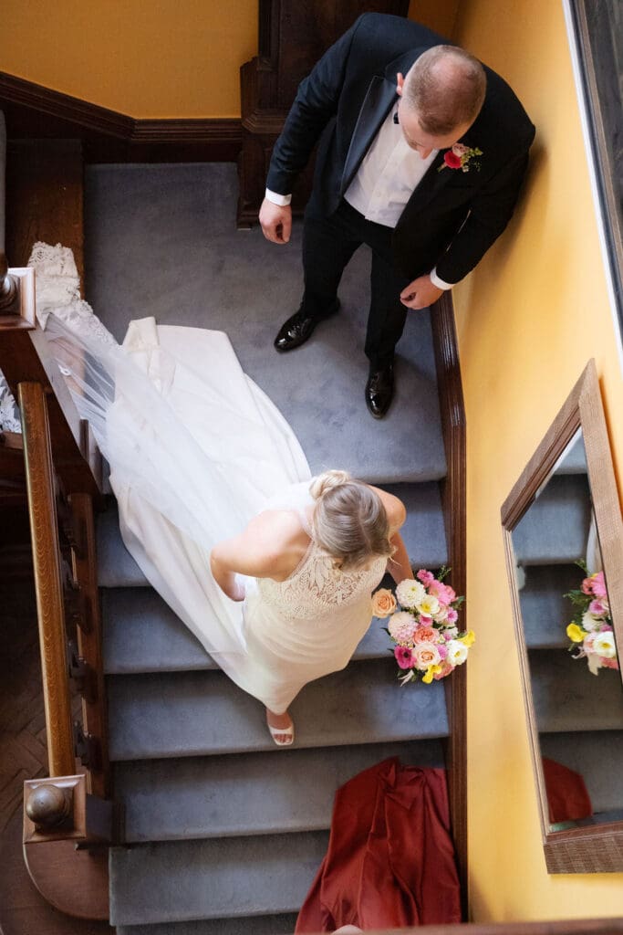 Bride in her veil walking down the staircase at Cissbury House, seen from above, as her brother waits at the bottom