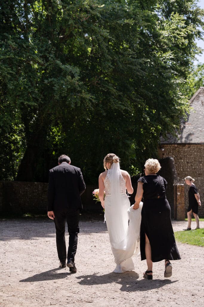 Bride walking across the gravel towards the barn with the groom and a guest after the ceremony