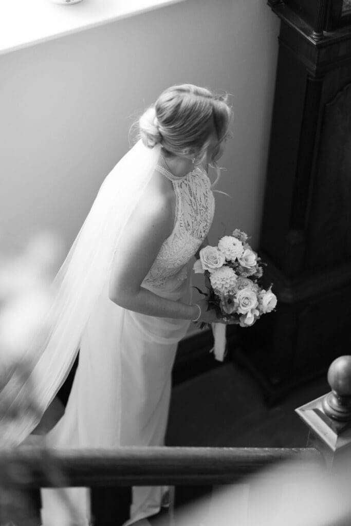 Black and white photo of the bride holding her bouquet as she pauses on the staircase at Cissbury House