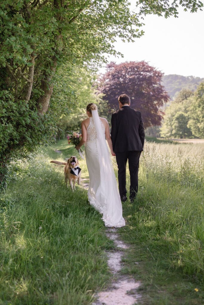 Bride and groom on a woodland path with their Labrador trotting alongside them