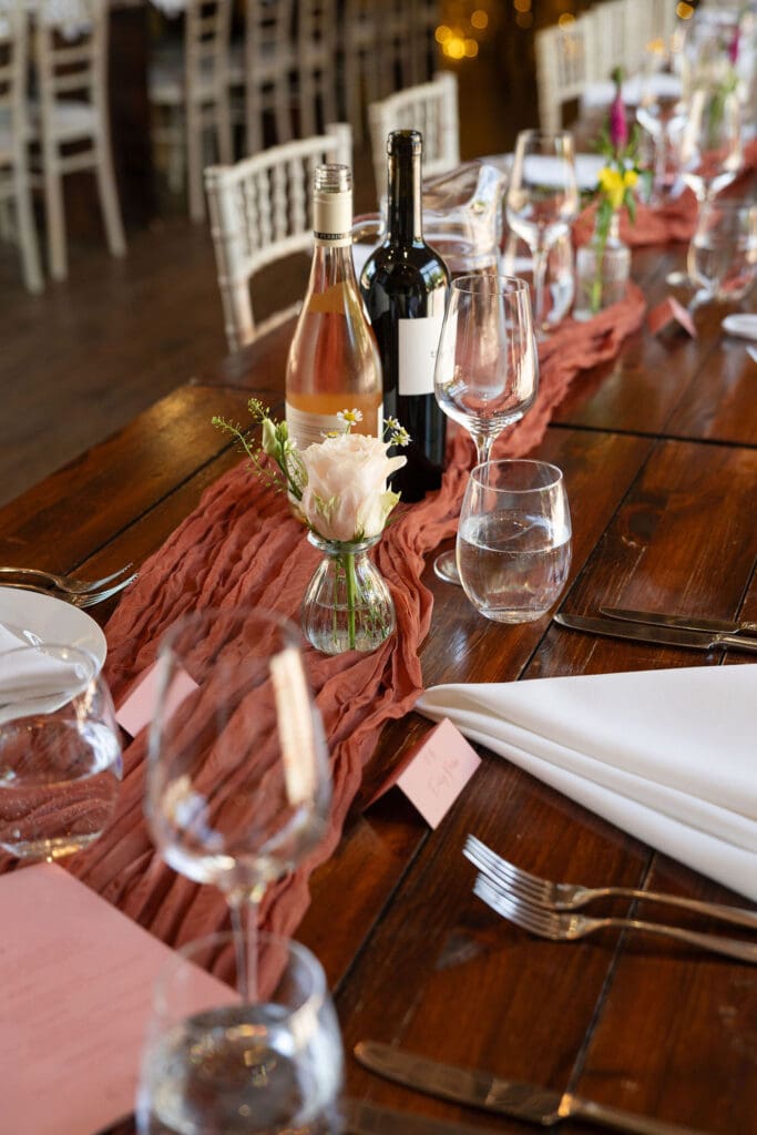 Table setting with a rust runner, glassware and flowers inside the barn